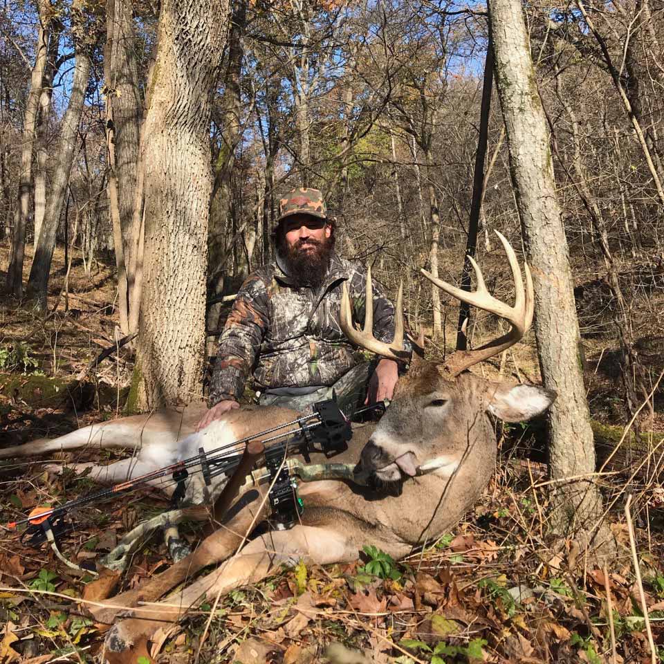 Hunter with buck and bow in woods