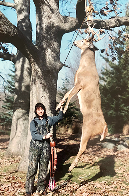 Renee Florent with bow and arrows wtih buck next to her hanging in tree